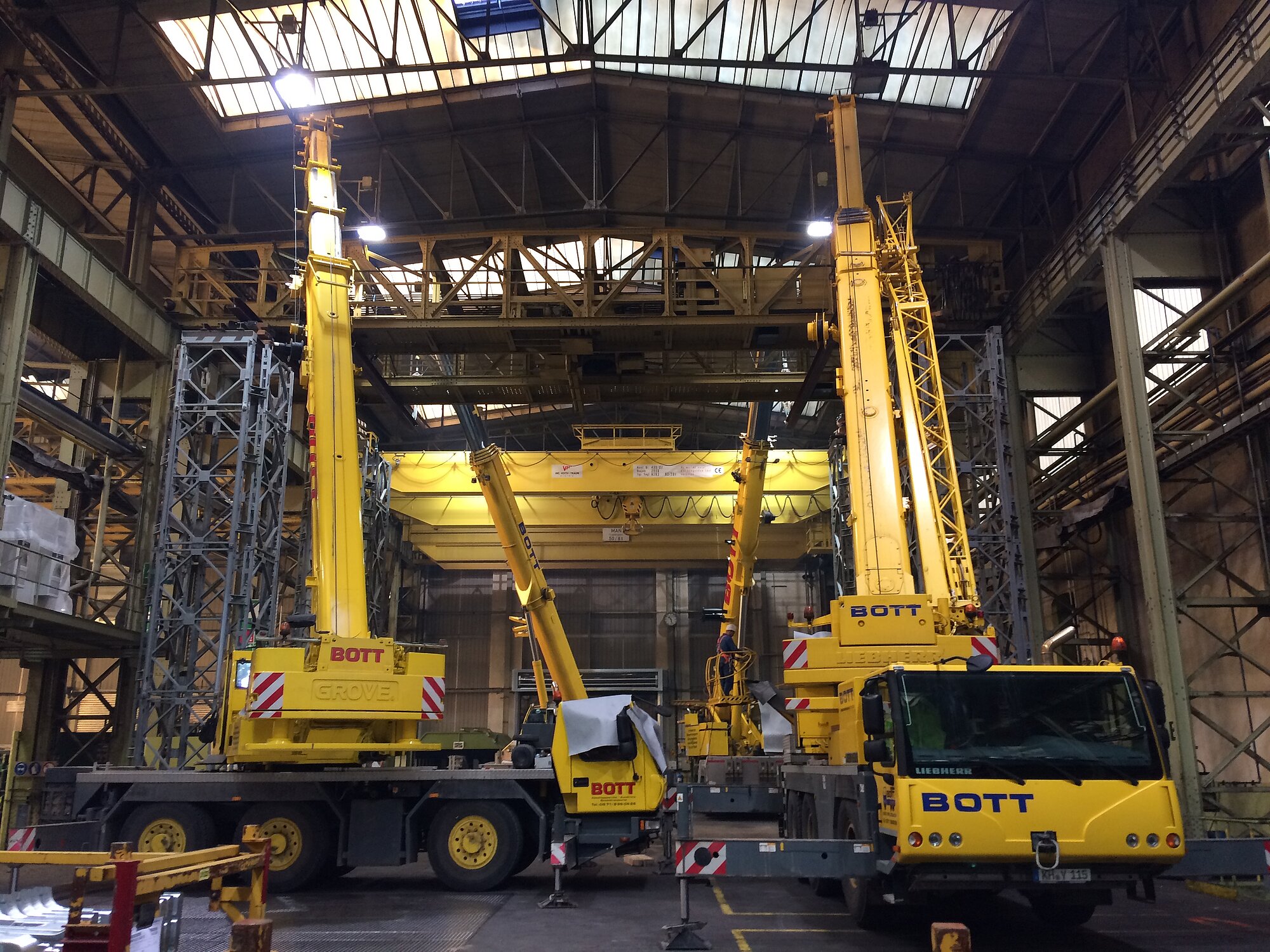Geparkte Mobilkräne in Industriehalle, einige mit teilweise ausgefahrenem Arm